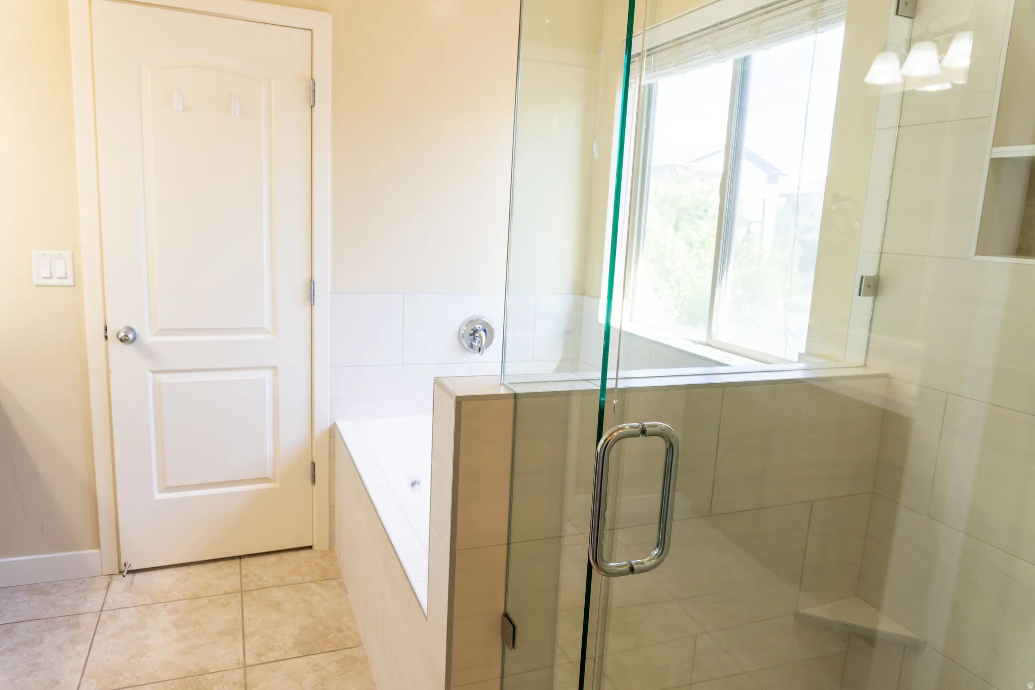 Glass-enclosed shower with a built-in bench, adjacent soaking tub, tiled flooring, and a large window