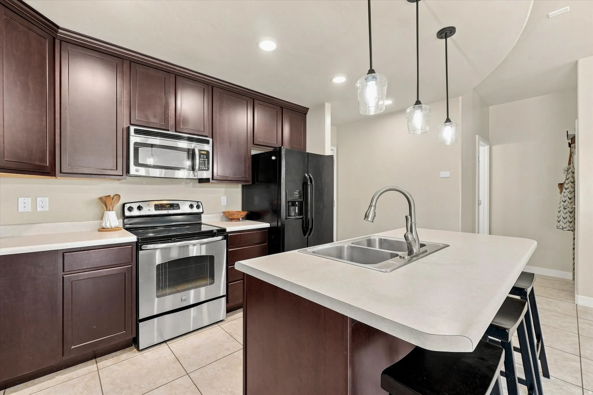 Kitchen featuring dark wood-finish cabinetry, stainless steel appliances, light-toned countertops, a dual basin sink, and pendant lighting