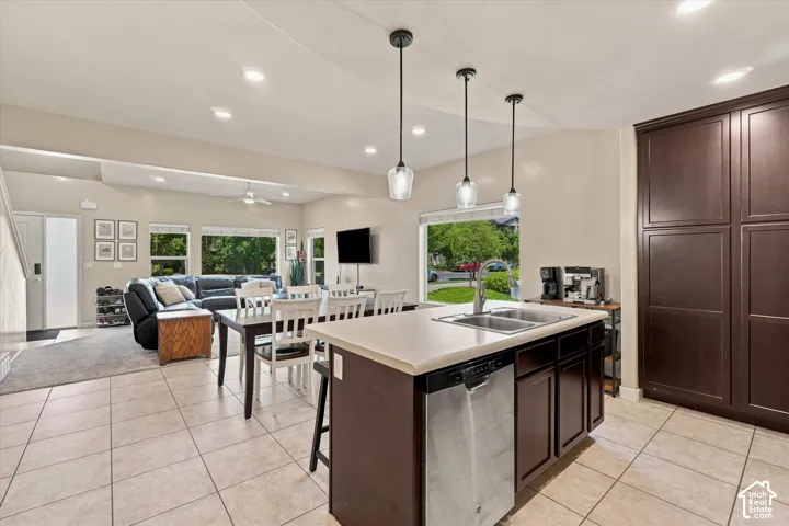 Kitchen island with a double basin sink and integrated dishwasher, dark wood-finish cabinetry, and tiled flooring