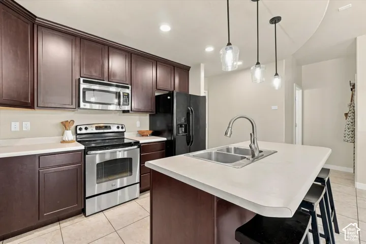 Kitchen featuring dark wood-finish cabinetry, stainless steel appliances, light-toned countertops, a dual basin sink, and pendant lighting