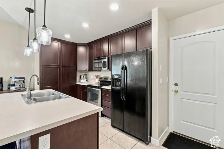 Kitchen featuring dark wood-finish cabinetry, stainless steel appliances, a double basin sink, and pendant lighting