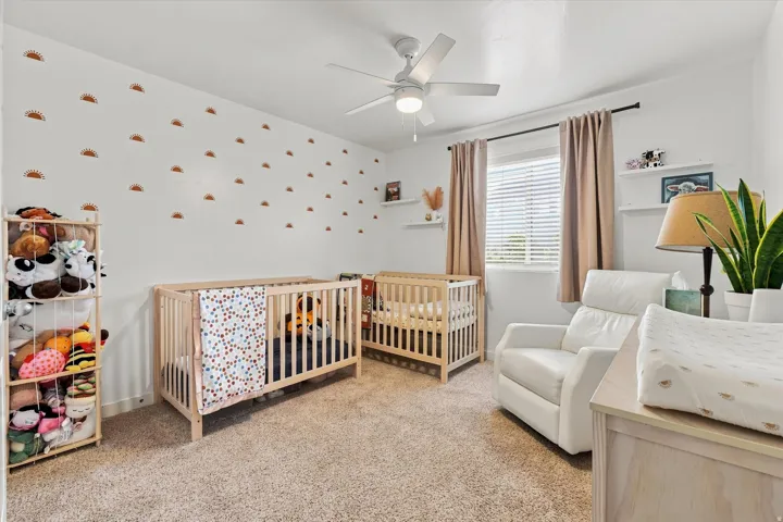 Carpeted flooring, white walls, ceiling fan, window with blinds, and floating shelves