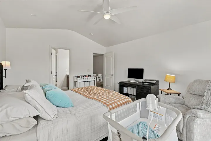 Vaulted ceiling with a ceiling fan, white walls, and a desk