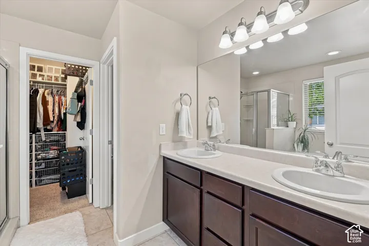 Dual vanity with integrated sinks, expansive wall mirror, dark wood-finish cabinetry, and a walk-in closet with built-in shelving