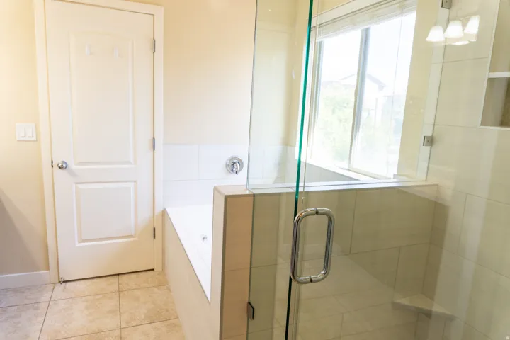 Glass-enclosed shower with a built-in bench, adjacent soaking tub, tiled flooring, and a large window
