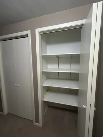 Built-in shelving with adjustable white shelves, white bi-fold closet doors, and light neutral-toned wall paint