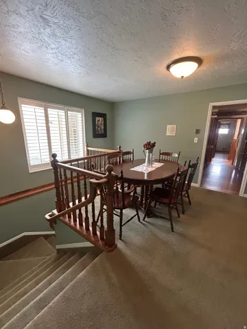 Carpeted staircase with wooden banister and spindles, featuring a decorative light fixture and window with plantation shutters