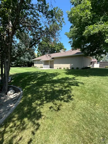 Expansive lawn surrounding the stucco exterior, featuring mature trees providing natural shade and a covered patio area