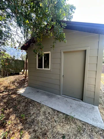 Exterior structure featuring horizontal siding, a single window, a solid entry door, a sloped roofline, and a concrete pad