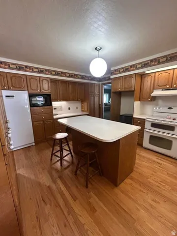 Spacious kitchen featuring wood cabinetry, a large center island with white countertop, stainless steel appliances including double wall ovens, and warm wood-finish flooring throughout
