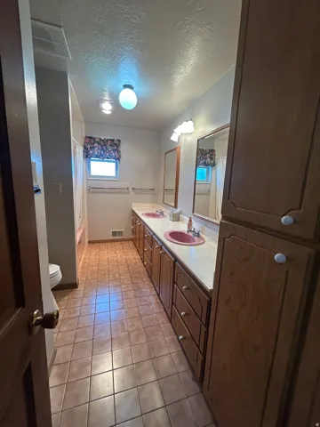 Dual vanity with integrated sinks, wood-finish cabinetry, tile flooring, and integrated storage tower