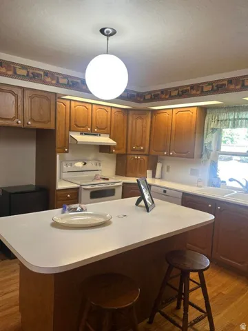 Kitchen featuring wood-finish cabinetry, white countertops, built-in white appliances, and a central island