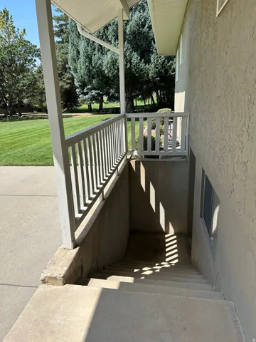 Covered exterior entry with white railing and concrete steps, featuring a stucco finish on the exterior wall