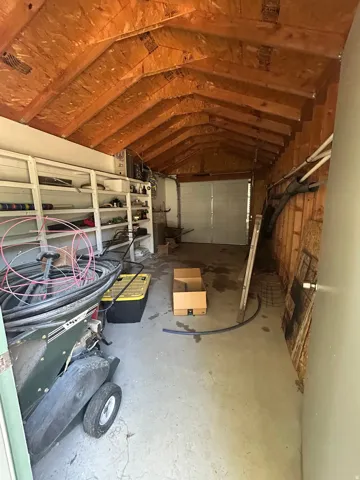 Exposed wood beam ceiling, concrete flooring, built-in shelving, wood wall paneling, and a garage door