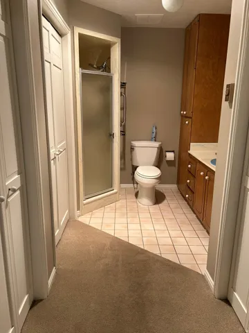 Enclosed shower with frosted glass door, tile flooring, built-in wooden cabinetry, and a vanity with an integrated sink