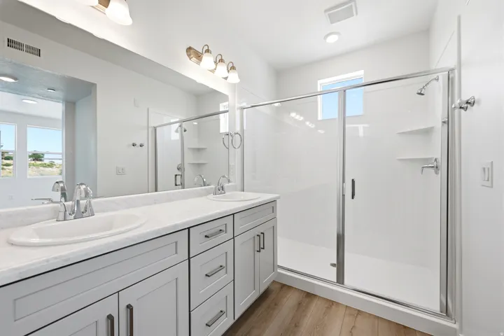 Dual vanity with undermount sinks, light wood-finish flooring, glass-enclosed shower, and built-in shower shelving