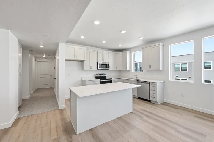Kitchen featuring light wood-finish flooring, white cabinetry, a center island with a white countertop, stainless steel appliances, and recessed lighting