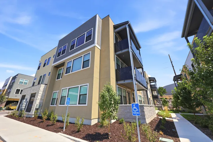 Modern multi-story building featuring balconies with metal railings, a facade with horizontal siding, and ground-level landscaping