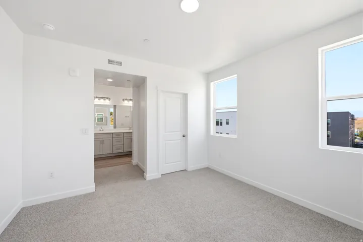 Spacious room with light-colored carpet, two windows, and a white paneled door