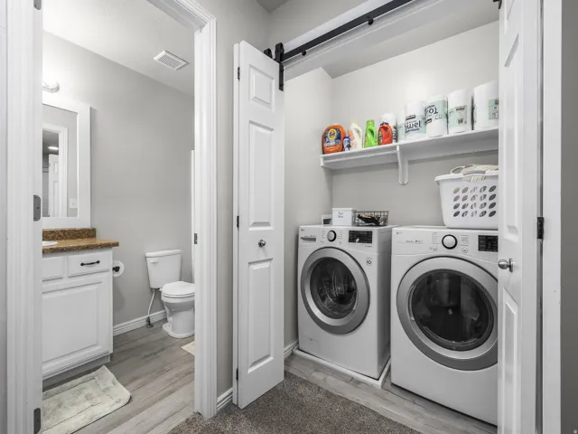 Dedicated laundry area with built-in shelving, front-loading appliances, wood-finish flooring, and a white barn door