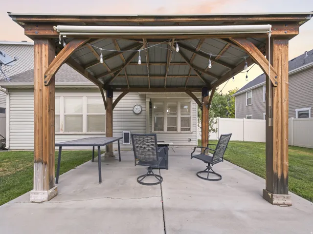 Covered patio with a wood-frame gazebo and metal roof, featuring a concrete pad and string lighting