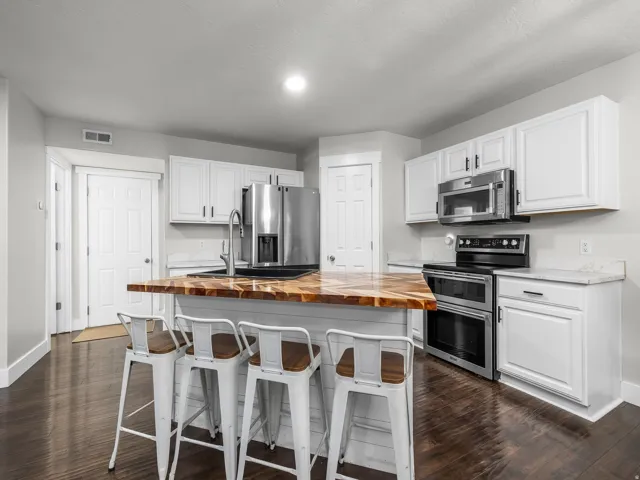 Hardwood-finish flooring, white cabinetry, stainless steel appliances, butcher block island countertop, and light-toned perimeter countertops