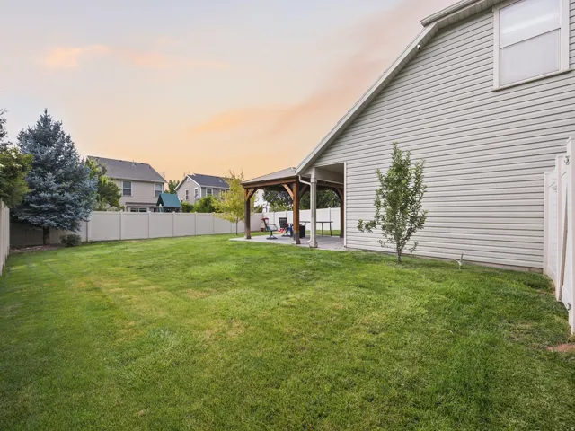 Expansive lawn area with a privacy fence, a covered patio structure, and a mature evergreen tree