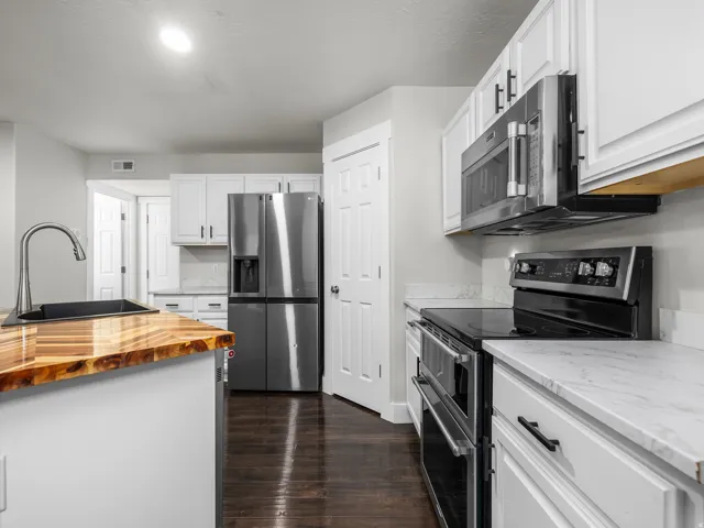 Kitchen featuring a wood-finish island countertop, stainless steel appliances, white cabinetry, a black kitchen sink, and dark wood-finish flooring
