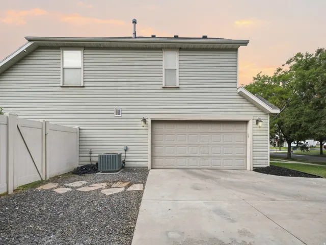 Two-story exterior with horizontal siding, attached garage, concrete driveway, and white privacy fencing