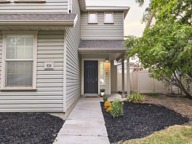 Exterior featuring light-colored siding, a covered entryway, mature landscaping, and a privacy fence