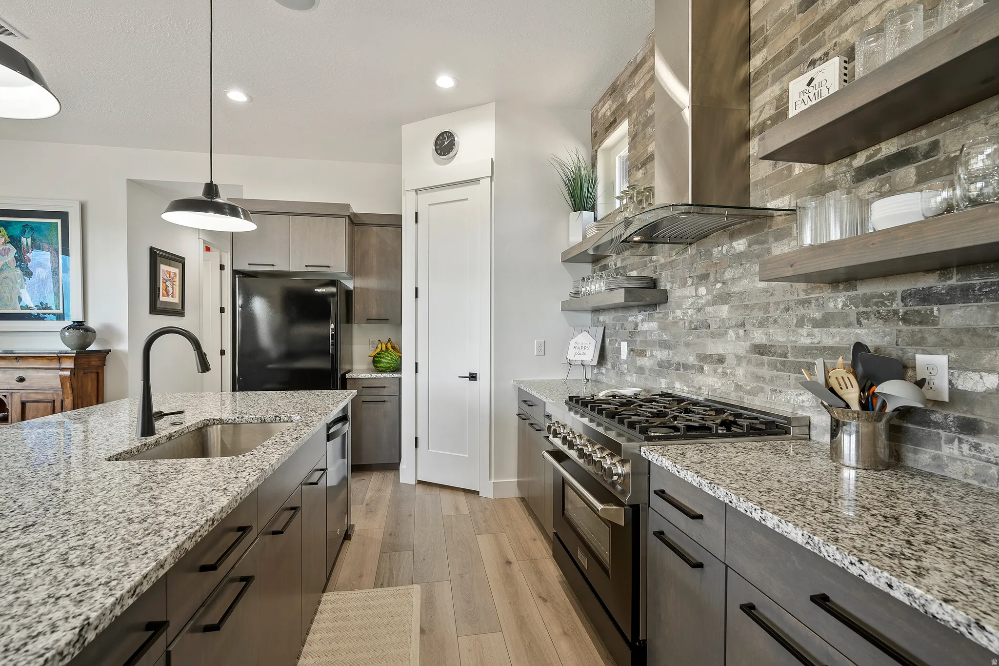Kitchen featuring granite countertops, wood-finish flooring, a stainless steel range with a ventilation hood, an integrated sink with a gooseneck faucet, and open shelving