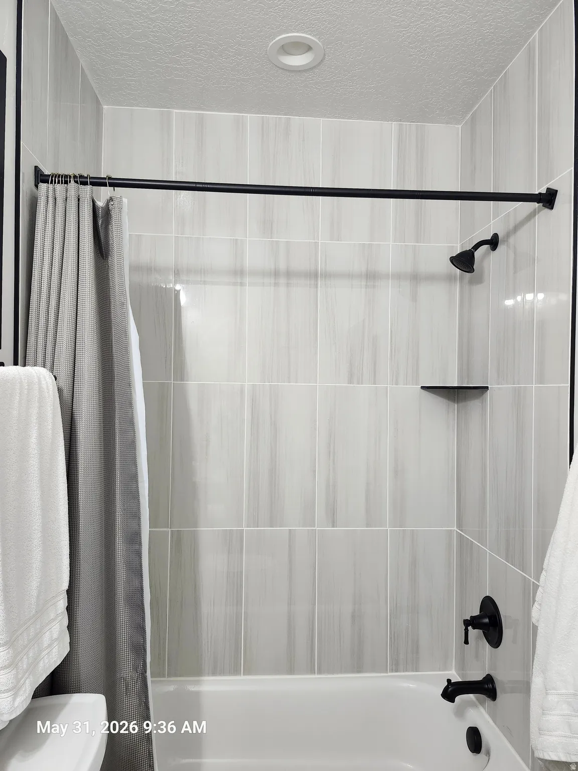 Bathtub and shower combination with vertical tile surround, matte black fixtures, and a recessed ceiling light