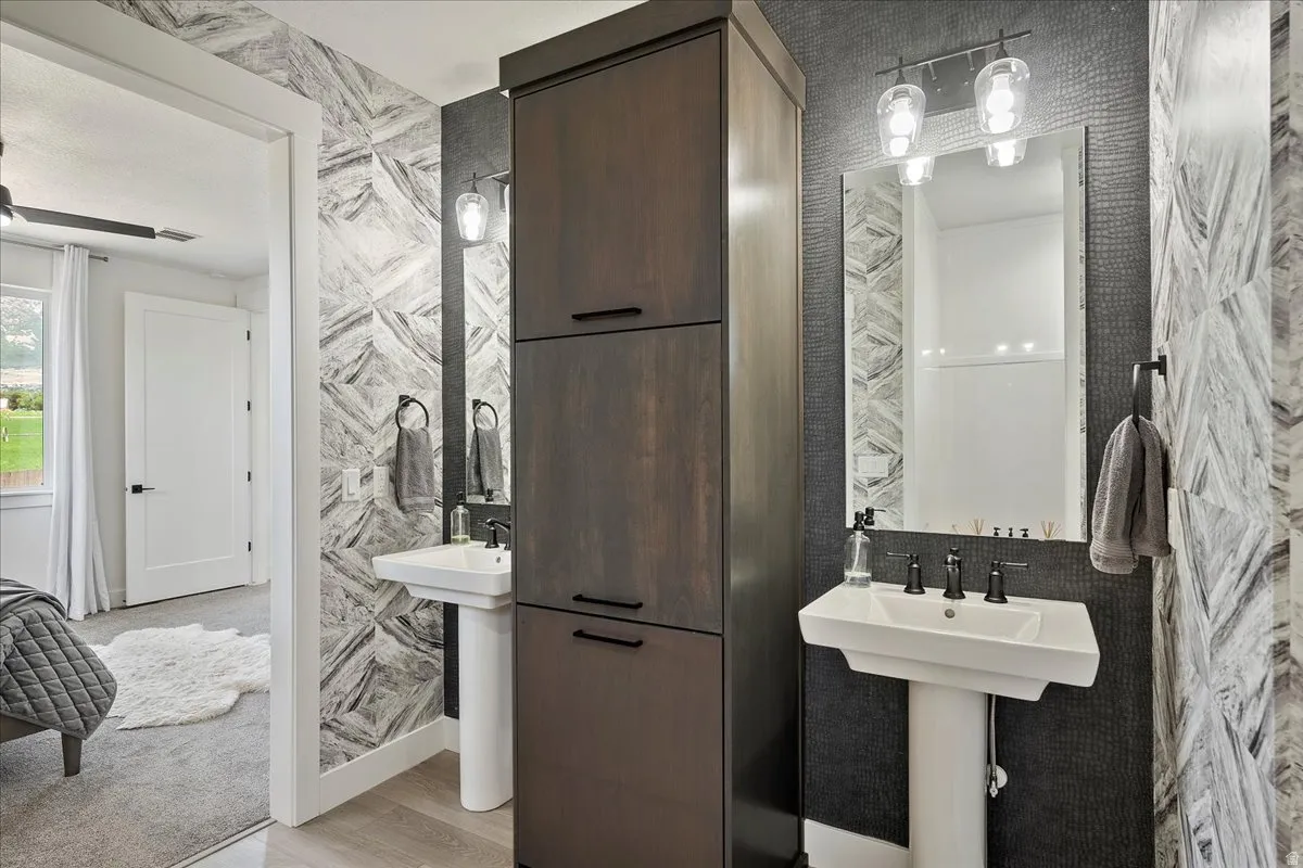 Pedestal sink with black-finish faucet, dark wood-finish storage cabinetry, and patterned wall tile