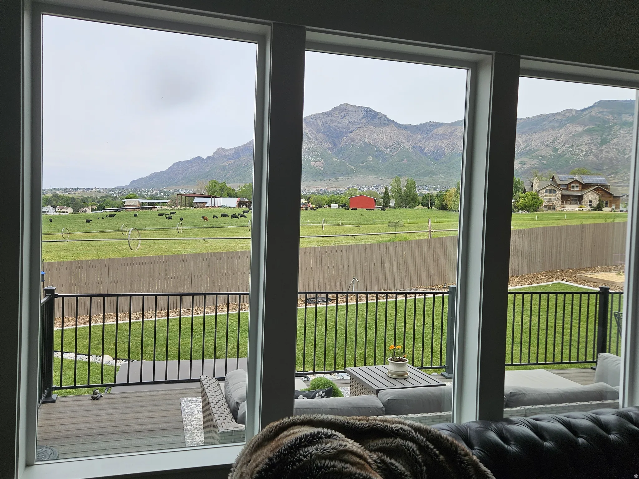 Expansive window wall with white frames, overlooking a composite deck with black metal railing, green lawn, and distant mountains