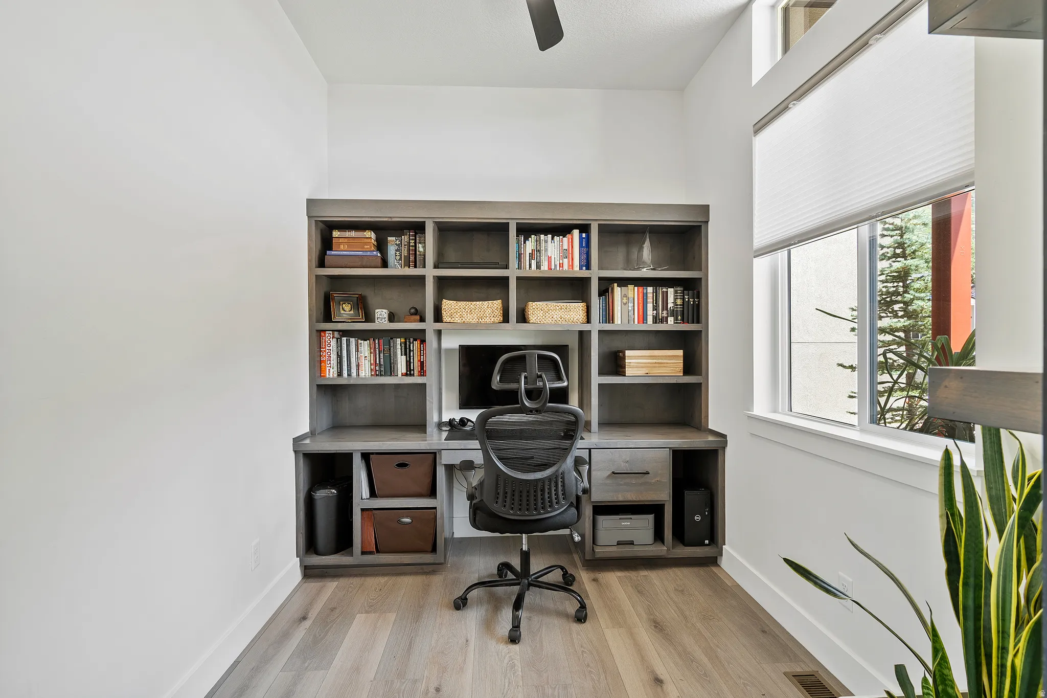 Built-in desk with integrated shelving, wood-finish flooring, and natural light from a large window
