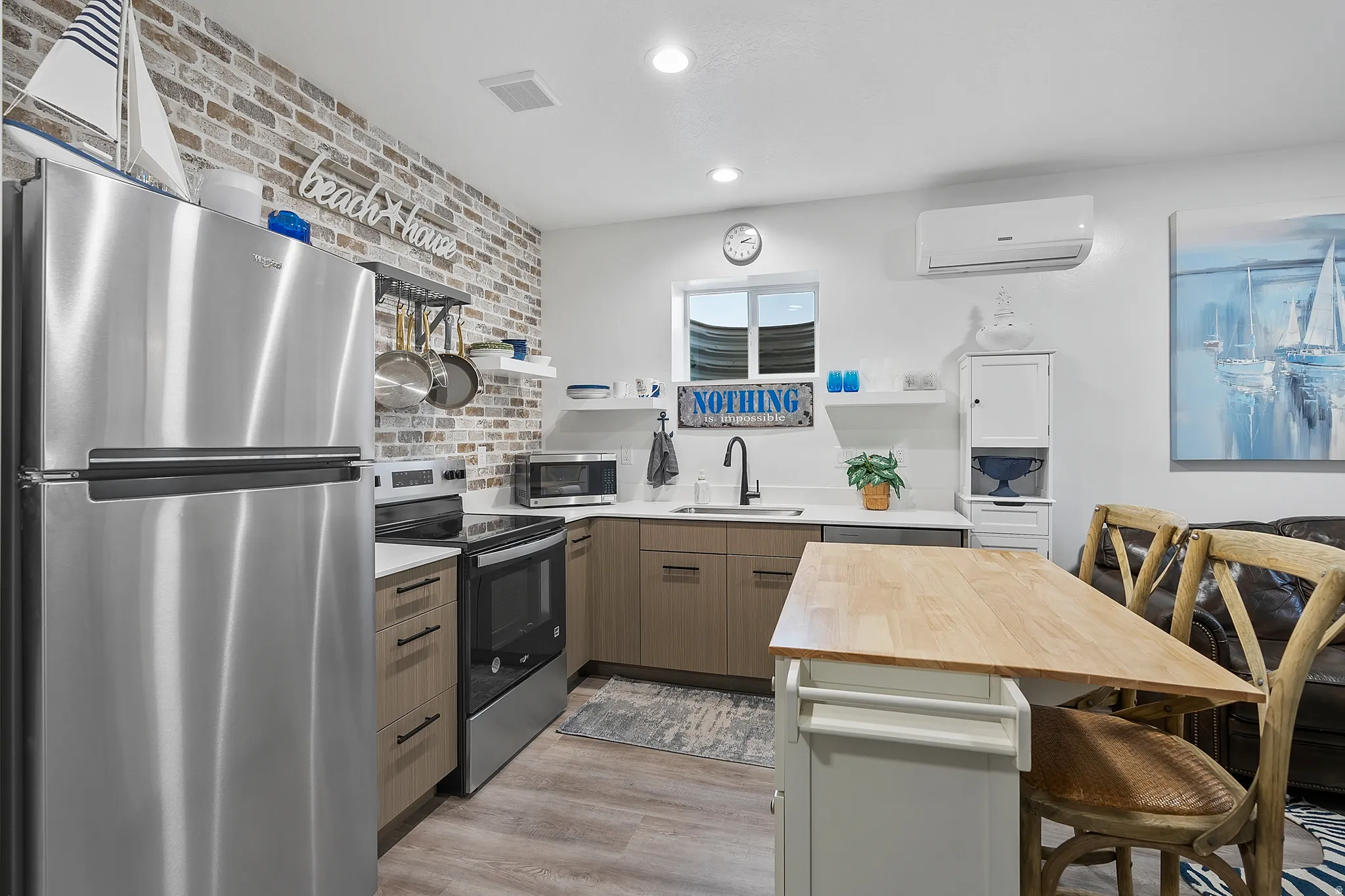 Stainless steel appliances, wood-finish flooring, light cabinetry, white countertops, and a white brick-look accent wall