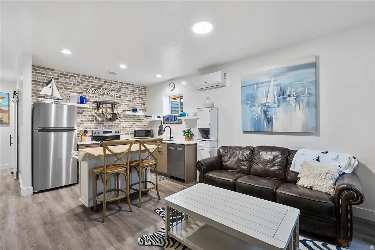 Recessed lighting, wood-finish flooring, brick-look accent wall, stainless steel appliances, and a built-in island with seating