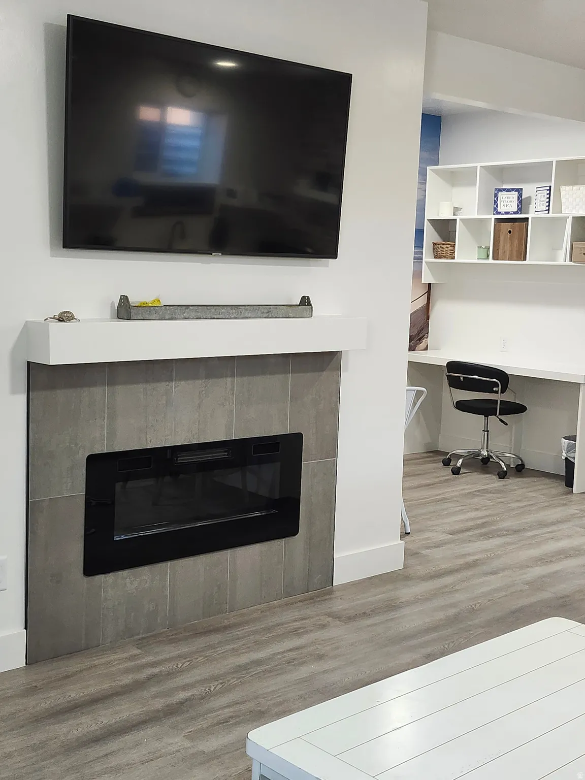 Modern electric fireplace with a tiled surround, white mantel, and wood-finish flooring