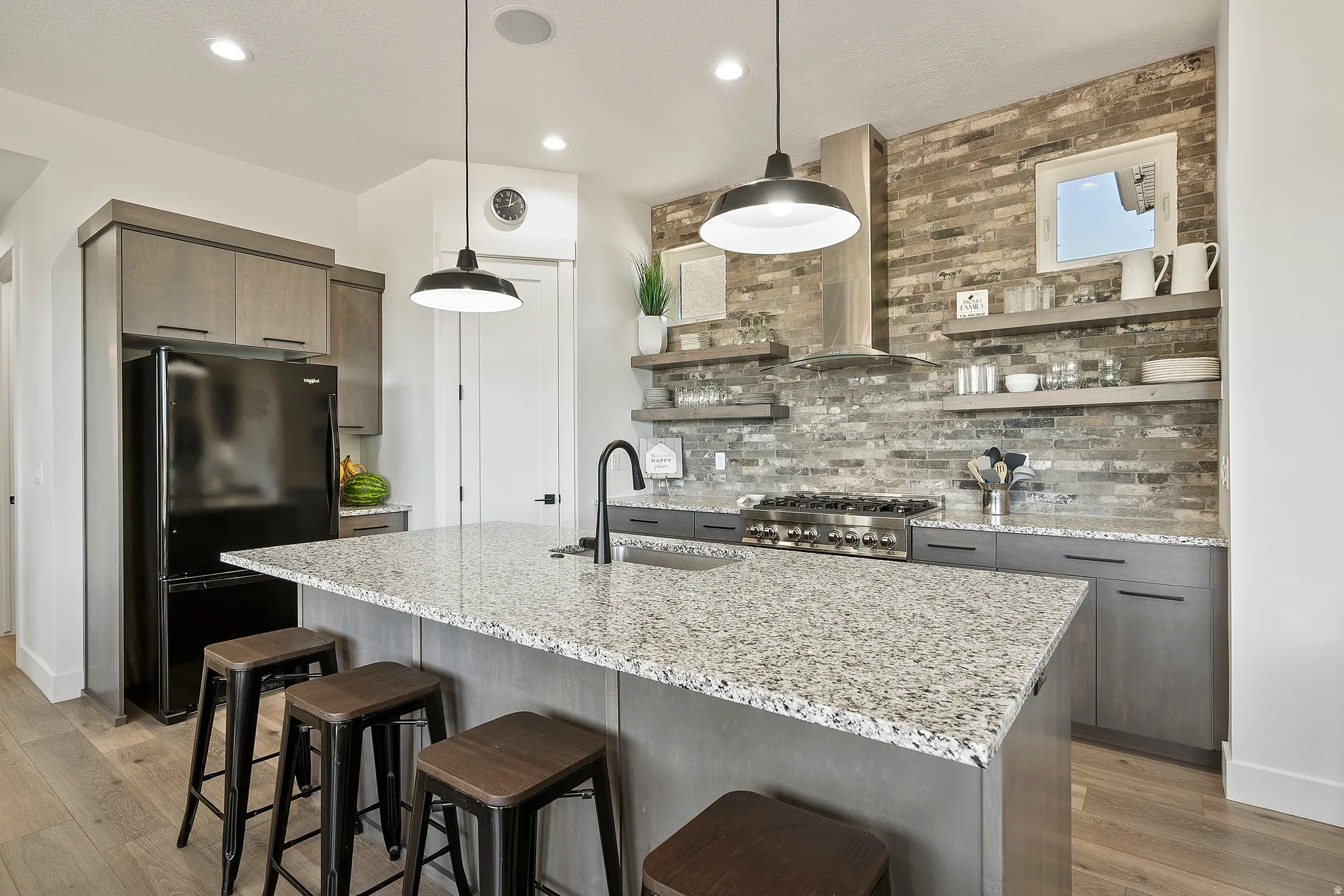 Kitchen featuring a large island with stone countertop, stainless steel range with hood, brick-finish backsplash, and wood-finish flooring