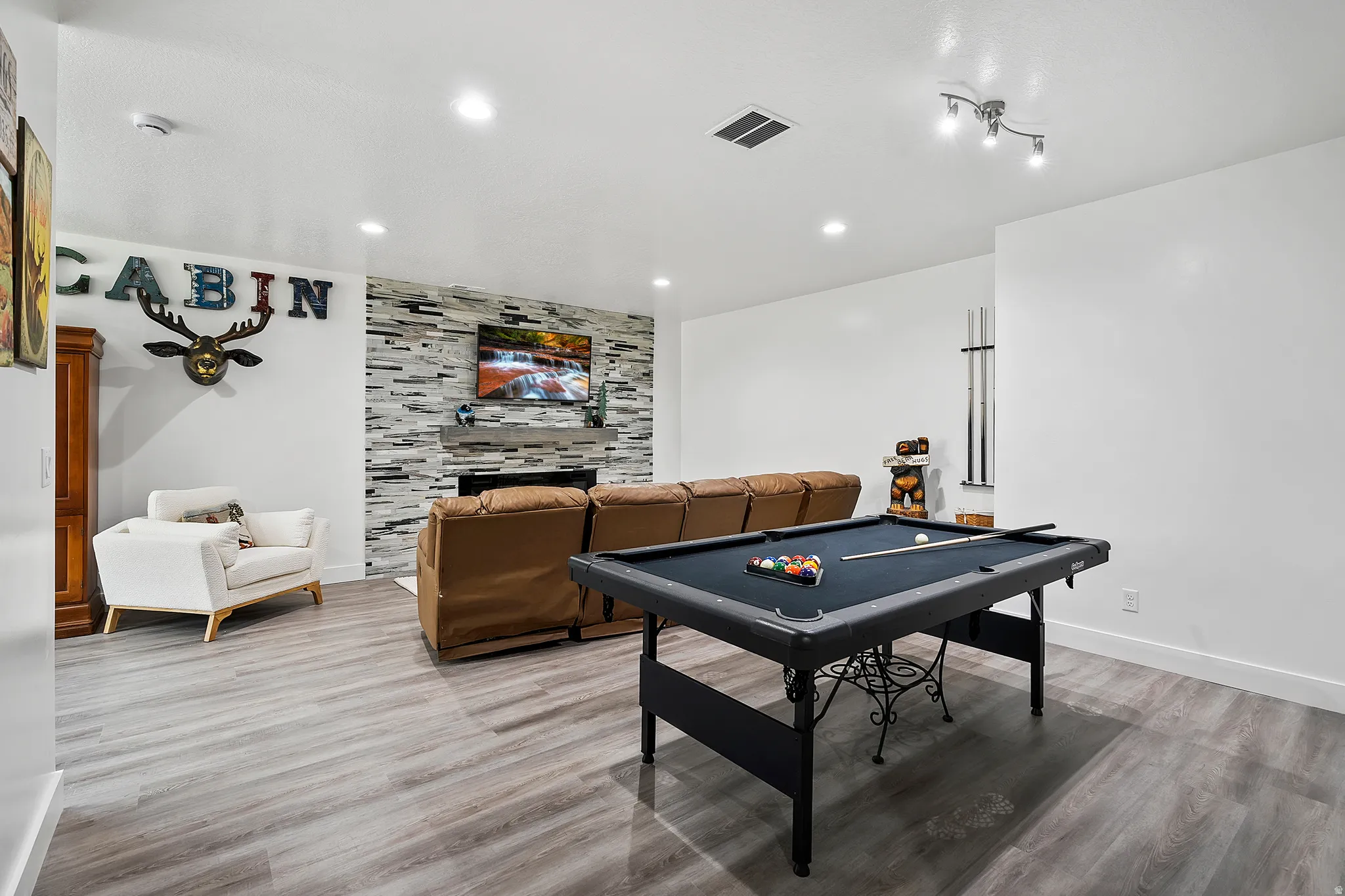 Recessed lighting, wood-finish flooring, and a fireplace with a stacked stone surround