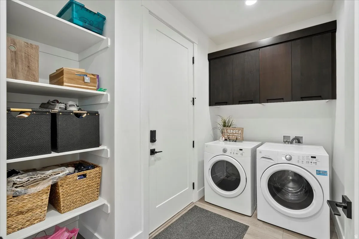Dedicated laundry area with built-in dark wood-finish cabinetry, white appliances, and light wood-finish flooring
