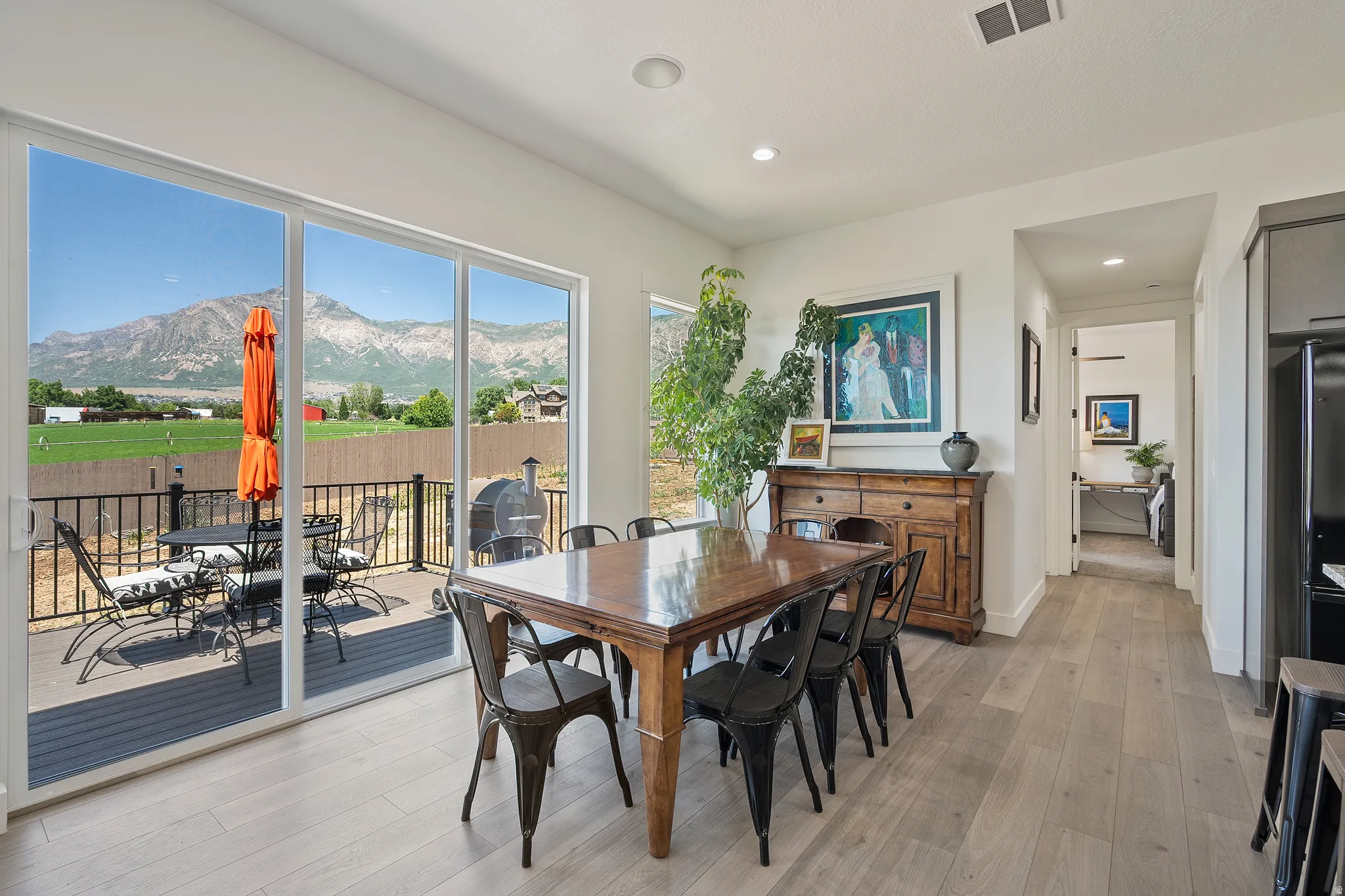 Expansive sliding glass doors, light wood-finish flooring, recessed ceiling lighting, and a composite deck with black metal railing