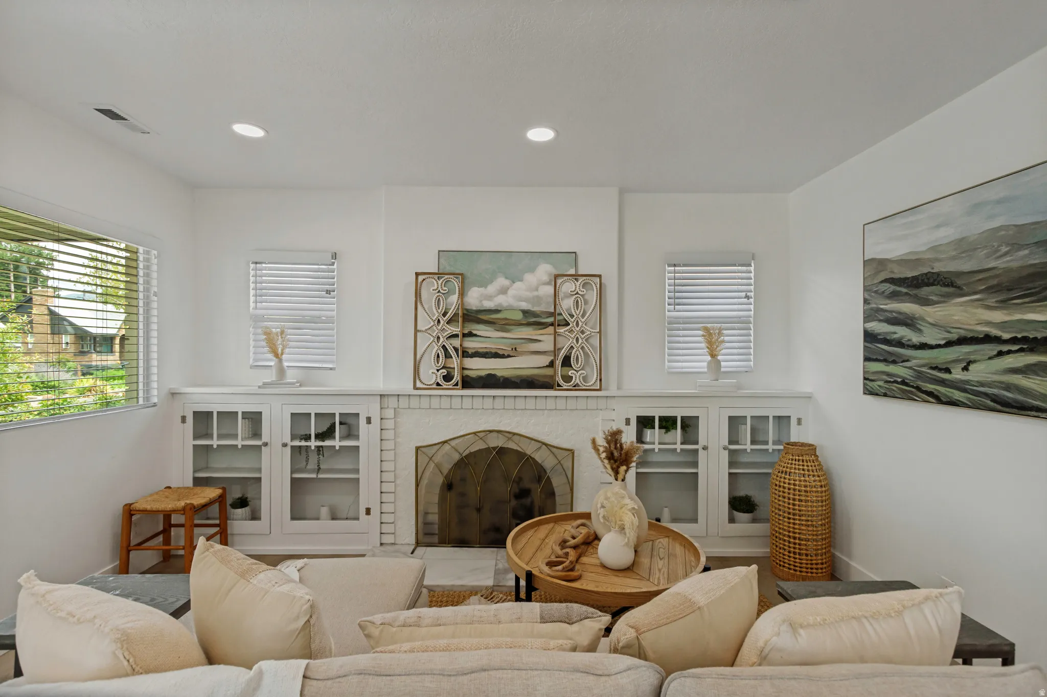 Fireplace with decorative screen, recessed lighting, built-in cabinetry with glass-front doors, and multiple windows providing natural light