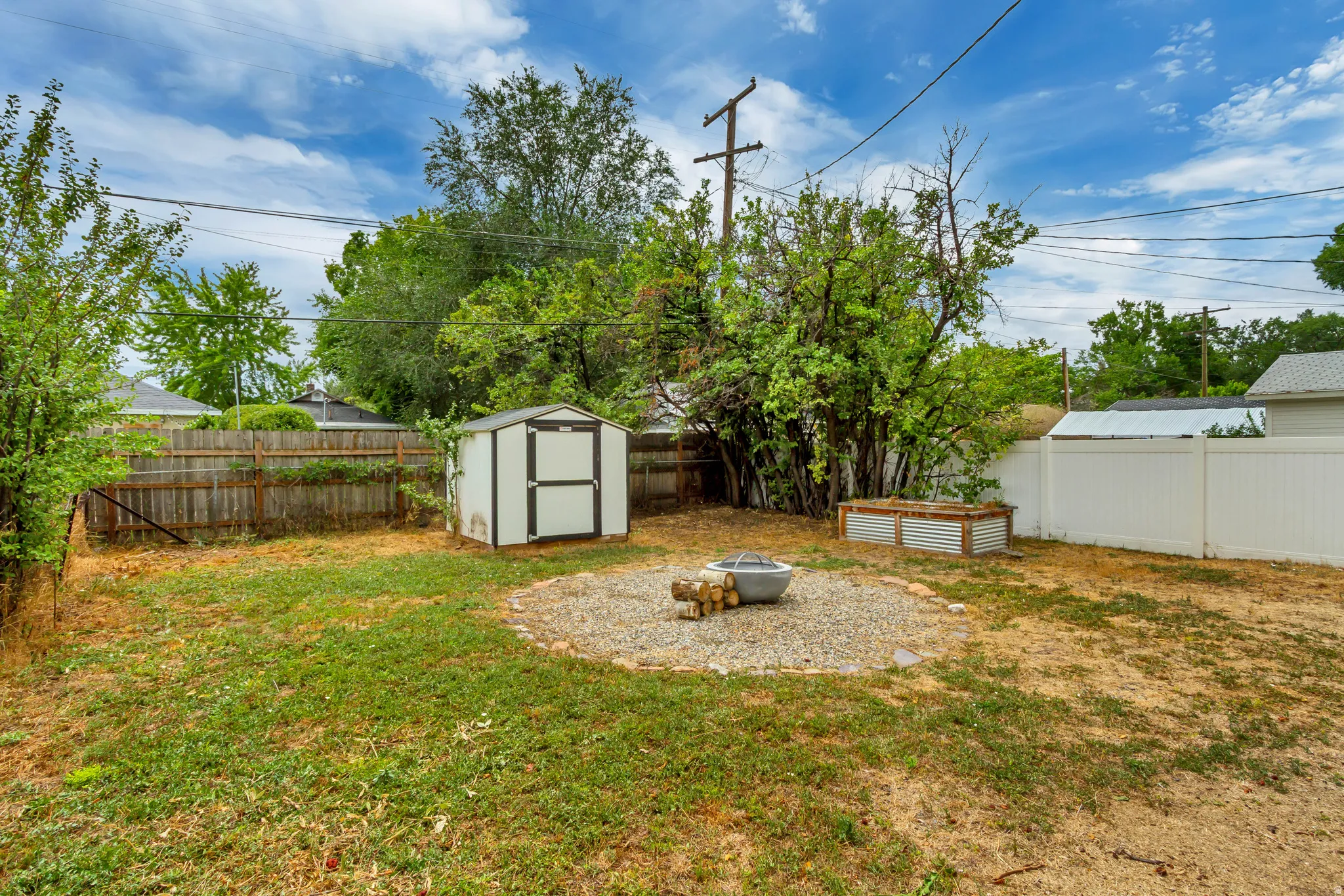 Expansive backyard featuring a gravel fire pit area, storage shed, raised garden beds, and privacy fencing