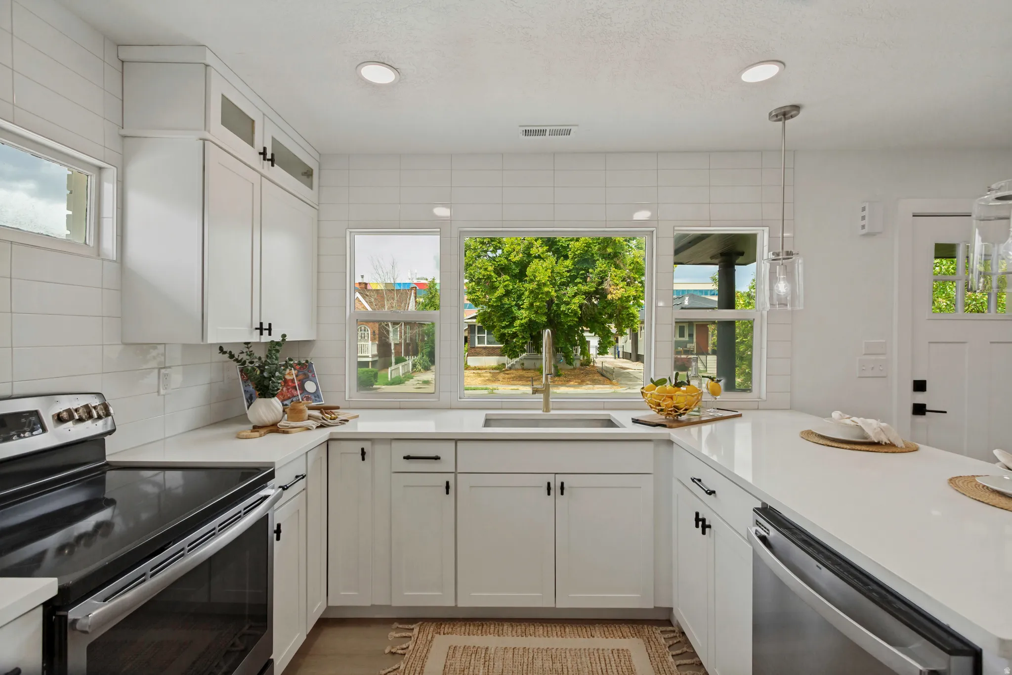 White cabinetry with matte black hardware, integrated stainless steel appliances, white subway tile backsplash, recessed lighting, and a window over the sink