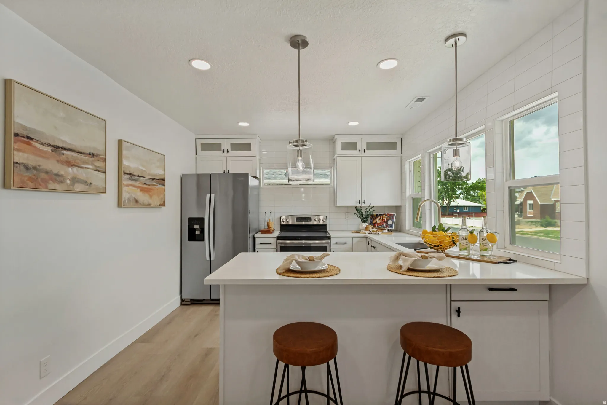 White shaker cabinetry, stainless steel appliances, wood-finish flooring, recessed lighting, and a white tile backsplash