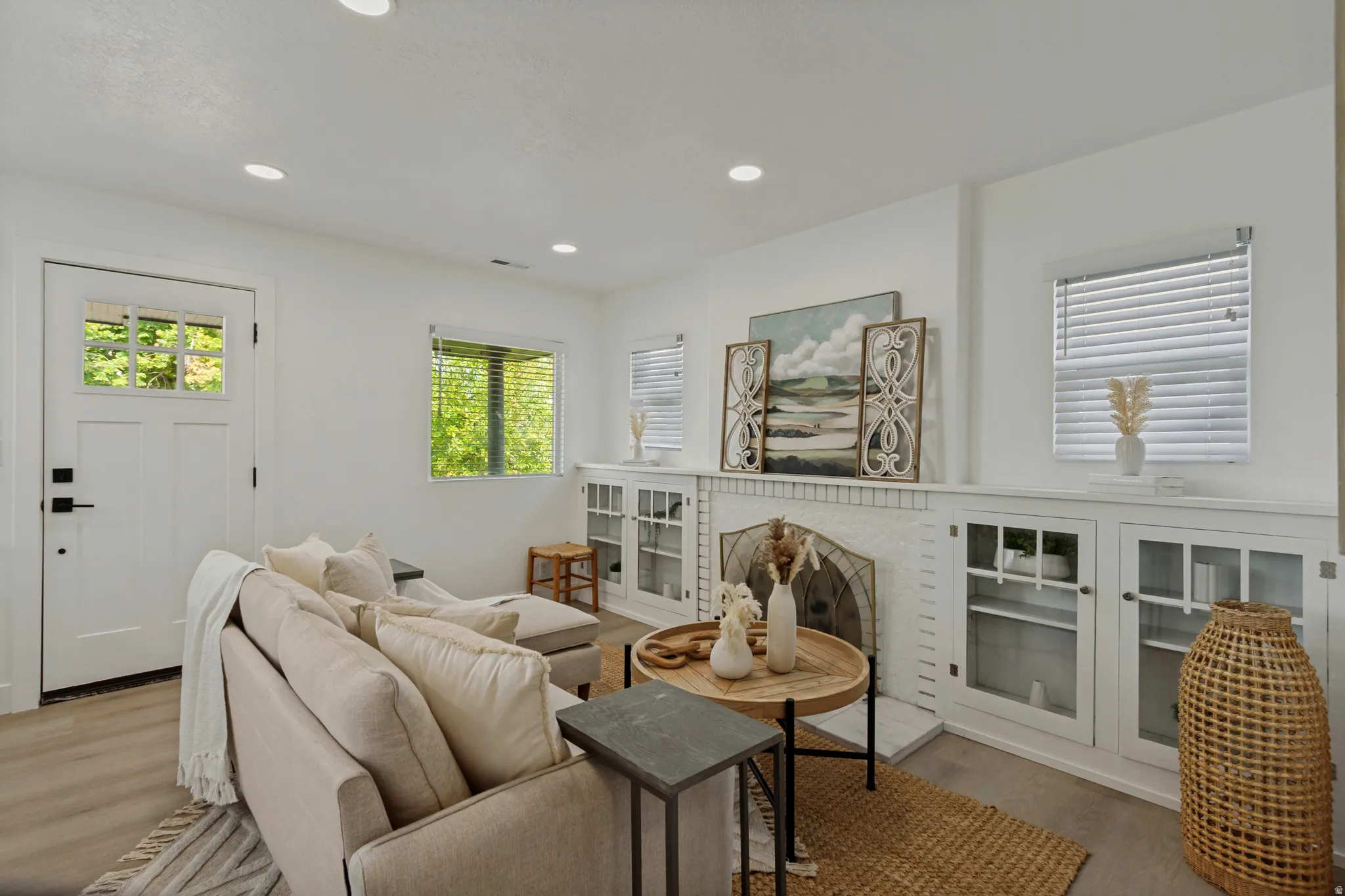 Recessed lighting, wood-finish flooring, white paneled door with glass inserts, fireplace with tile surround, and built-in cabinetry with glass doors