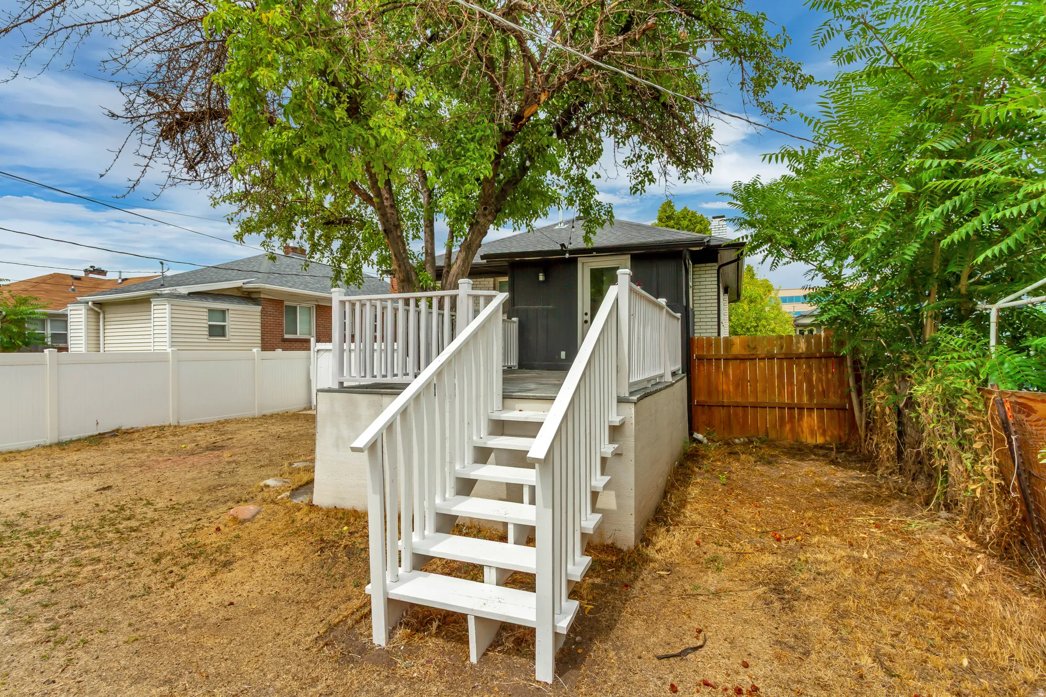 Rear yard featuring a white-painted wooden deck with steps and railing, mature tree, and a wooden privacy fence