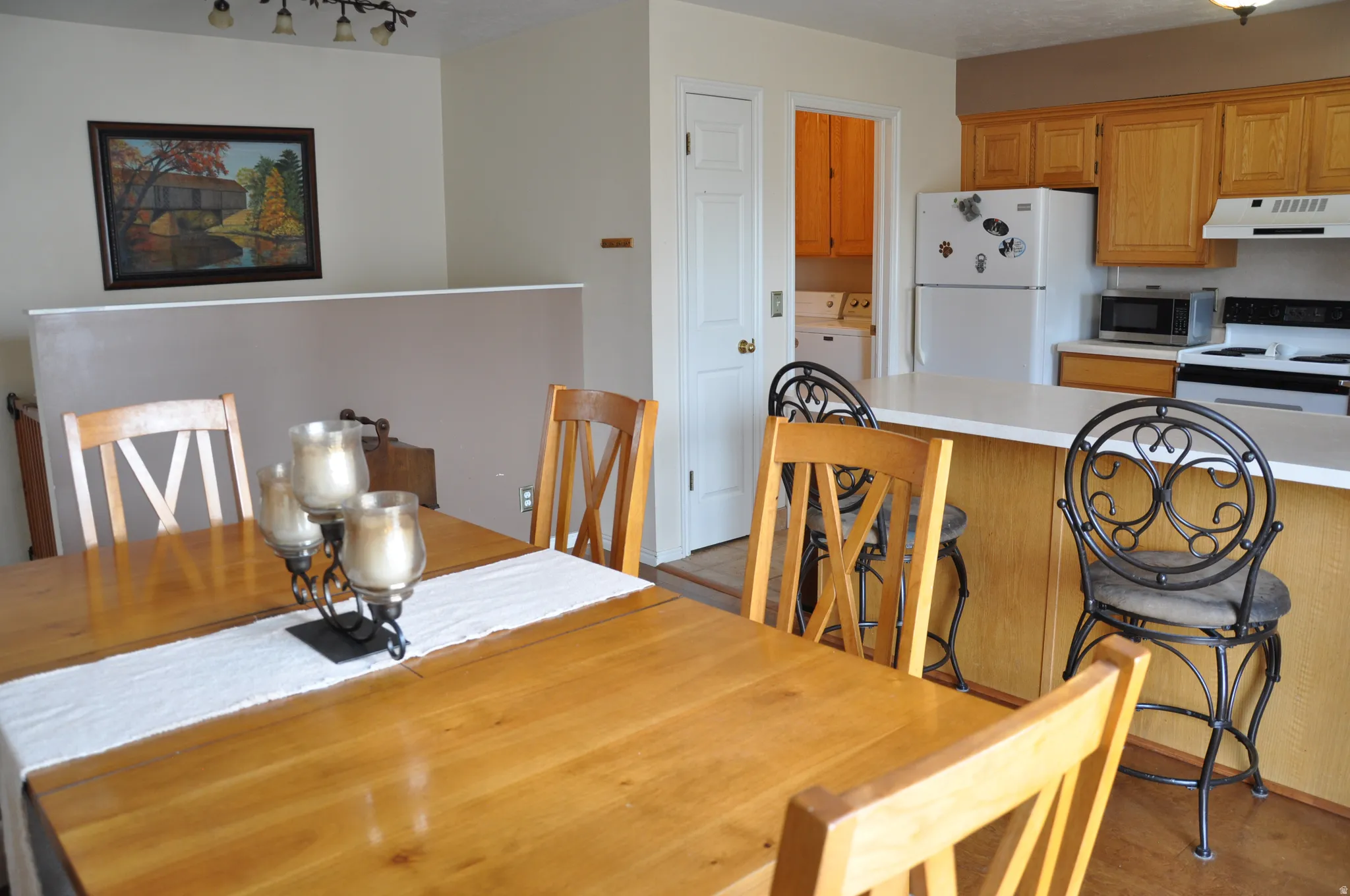 Kitchen featuring light wood-finish cabinetry, white appliances, and a breakfast bar with solid surface countertop