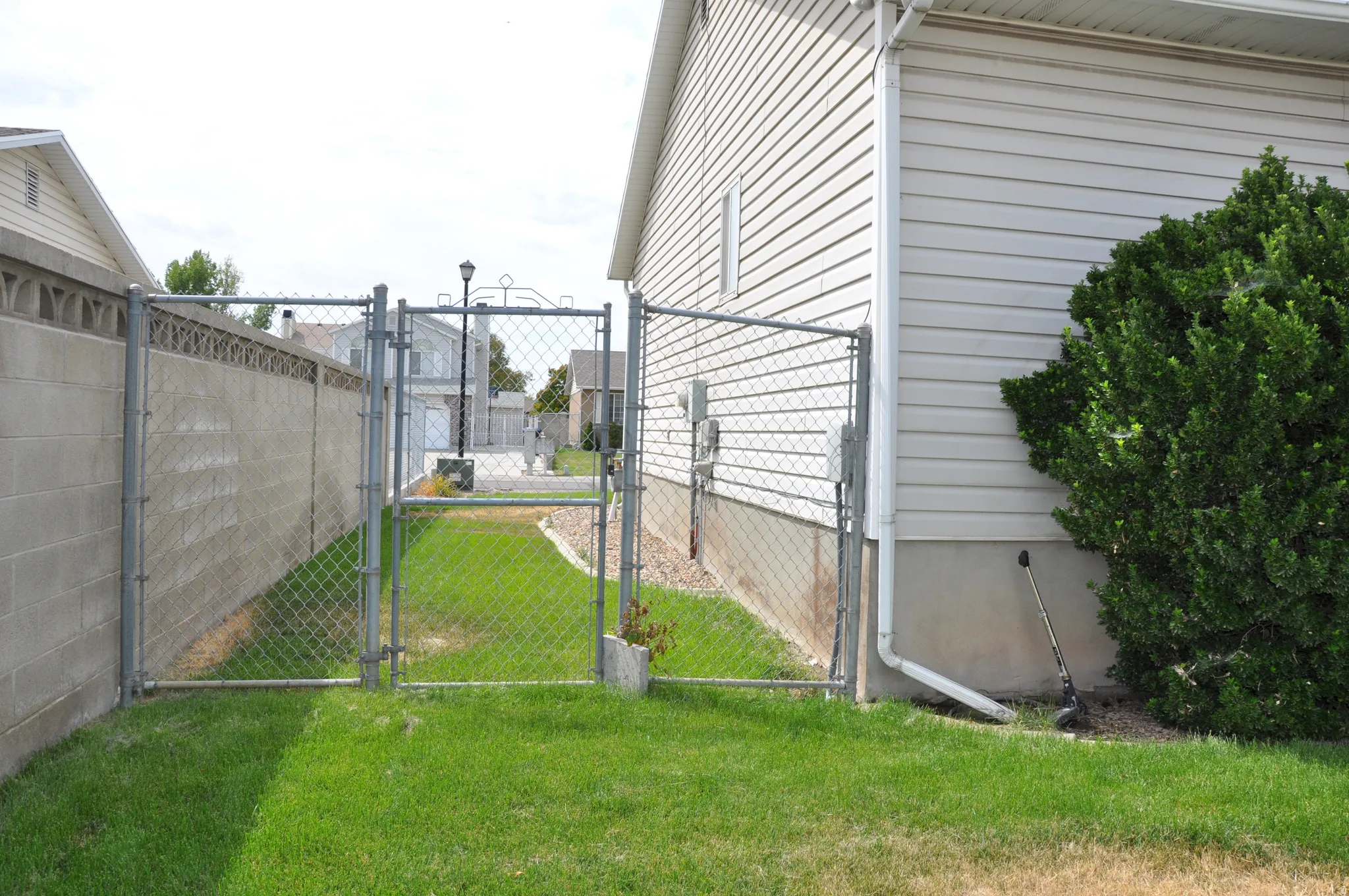 Chain link fence with a gate, concrete block wall, and manicured lawn